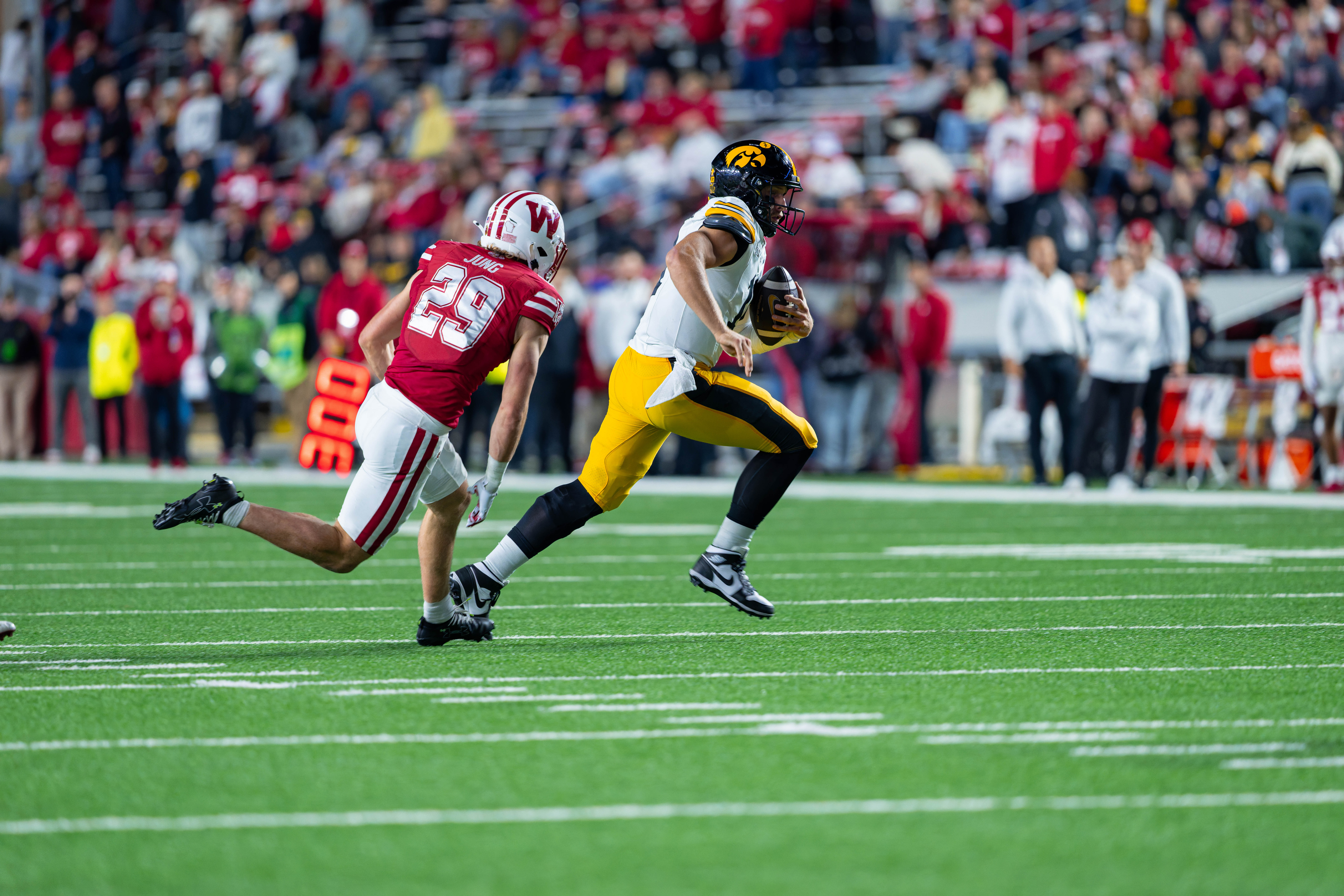 Oct 11, 2025; Madison, Wisconsin, USA; Iowa Hawkeyes quarterback Mark Gronowski (11) runs the ball in the second half while being chased by Wisconsin Badgers safety Matthew Jung (29) at Camp Randall Stadium. Mandatory Credit Photography by Ross Harried for Second Crop Sports.