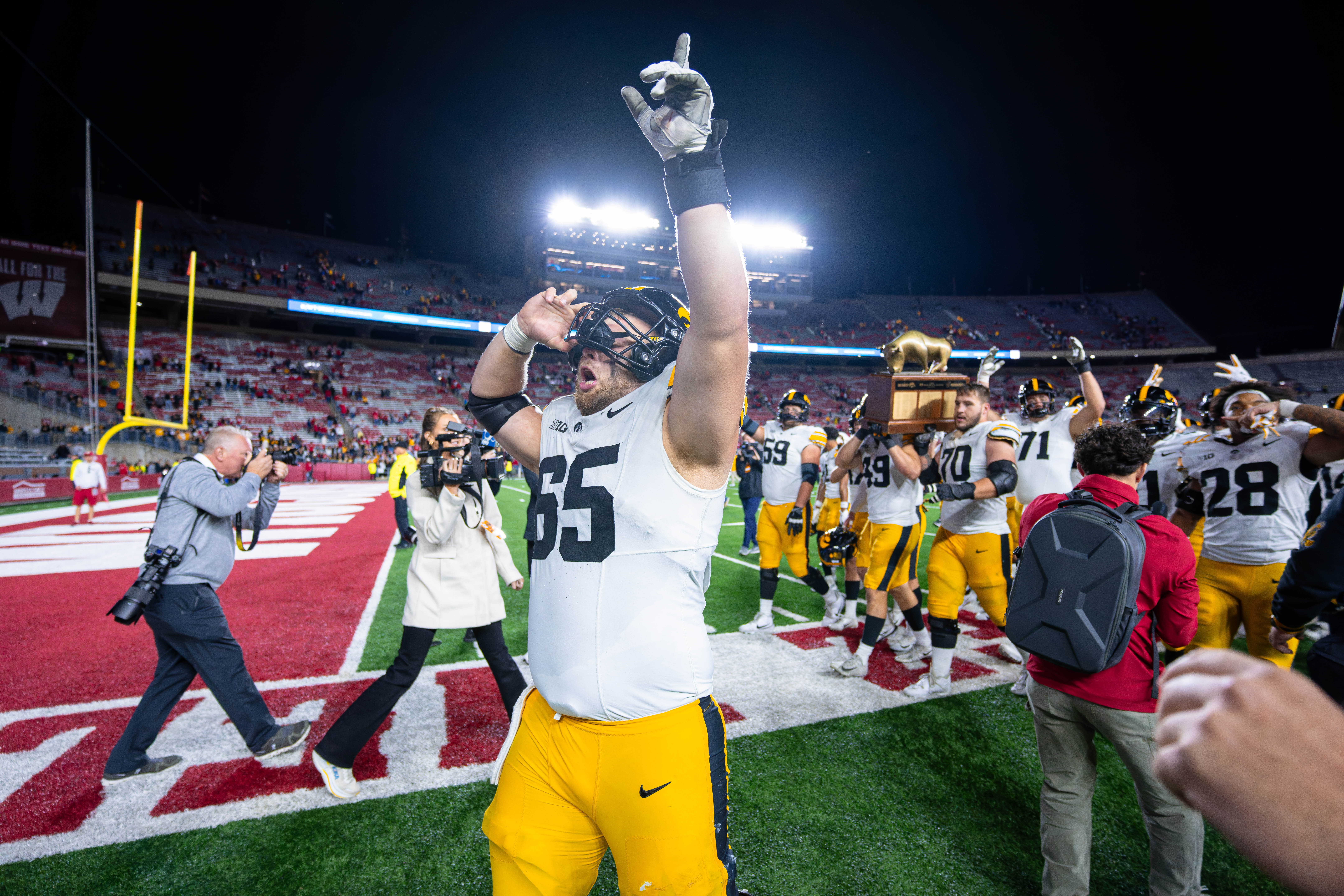Oct 11, 2025; Madison, Wisconsin, USA; Iowa Hawkeyes offensive lineman Logan Jones (65) celebrates a win against the Wisconsin Badgers while his teammates carry The Heartland Trophy in the background at Camp Randall Stadium. Mandatory Credit Photography by Ross Harried for Second Crop Sports.